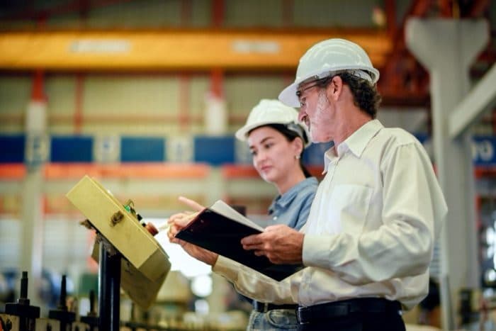 Two workers in hard hats reviewing work on the plant floor